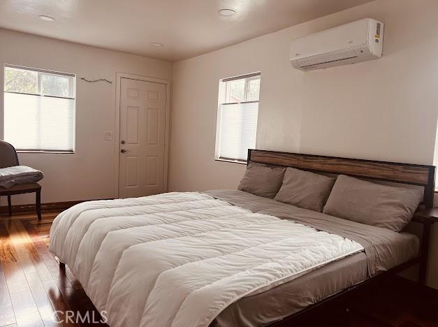 bedroom featuring hardwood / wood-style floors, multiple windows, and an AC wall unit