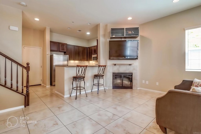 kitchen with light tile patterned floors, stainless steel fridge, a kitchen breakfast bar, kitchen peninsula, and a tile fireplace