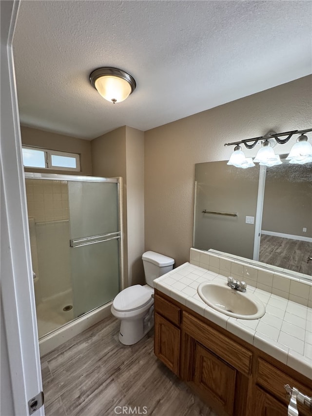 bathroom featuring hardwood / wood-style flooring, a shower with door, vanity, a textured ceiling, and toilet