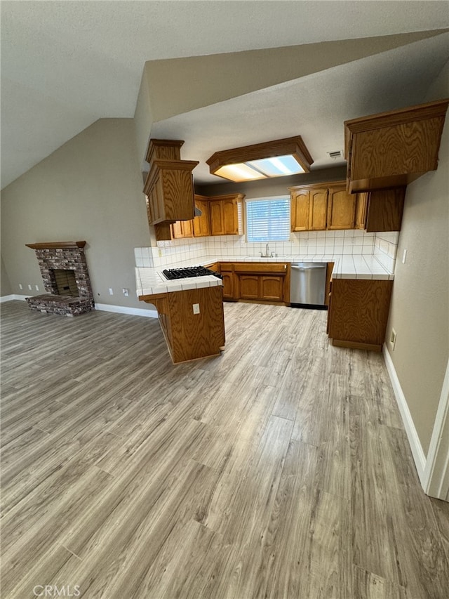 kitchen featuring vaulted ceiling, tile counters, dishwasher, light hardwood / wood-style floors, and decorative backsplash