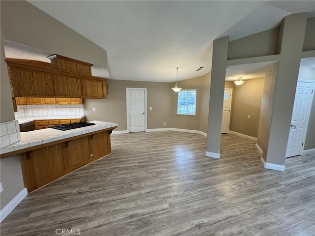 kitchen featuring tasteful backsplash, tile countertops, vaulted ceiling, light wood-type flooring, and kitchen peninsula