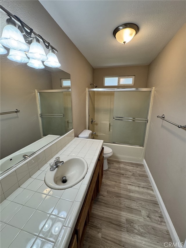 full bathroom with toilet, wood-type flooring, shower / bath combination with glass door, a textured ceiling, and vanity