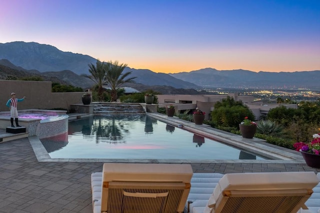 pool at dusk featuring an in ground hot tub, a mountain view, and a patio