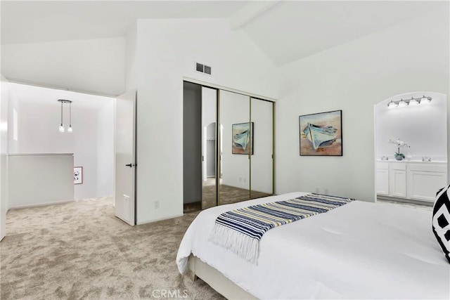 bedroom with high vaulted ceiling, connected bathroom, light colored carpet, a closet, and beamed ceiling