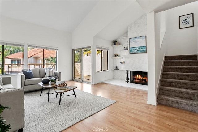 living room featuring a tiled fireplace, high vaulted ceiling, plenty of natural light, and light hardwood / wood-style floors