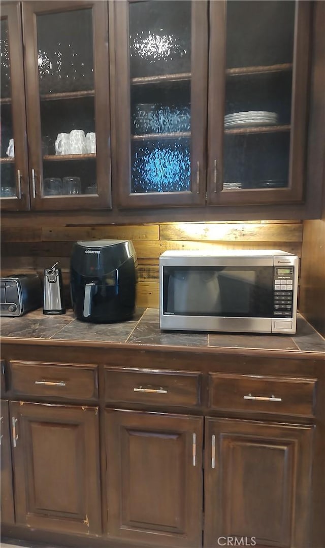 room details with dark brown cabinetry, stainless steel microwave, and tile countertops