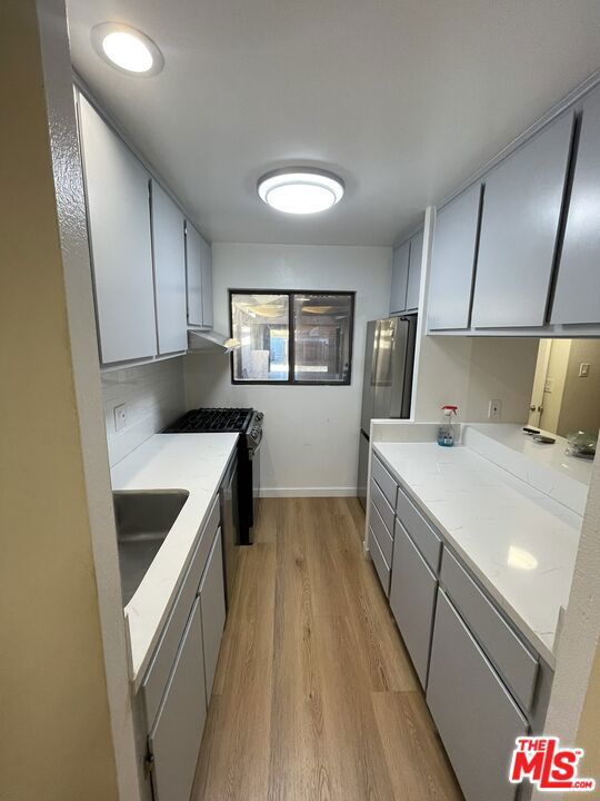 kitchen featuring gas stove, fridge, sink, and light hardwood / wood-style flooring