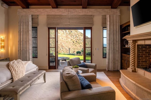 living room with beam ceiling, a tiled fireplace, hardwood / wood-style floors, and wooden ceiling