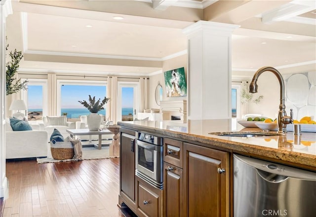 kitchen with sink, light stone counters, a water view, stainless steel dishwasher, and dark hardwood / wood-style floors