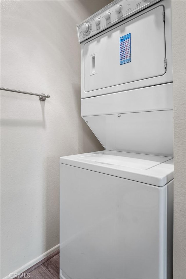 laundry area featuring baseboards, wood finished floors, laundry area, and stacked washer / dryer