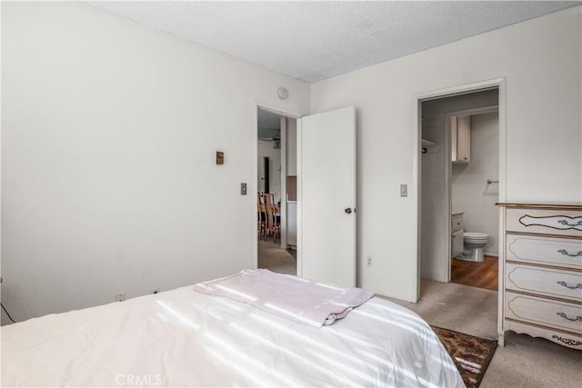 carpeted bedroom with ensuite bathroom and a textured ceiling