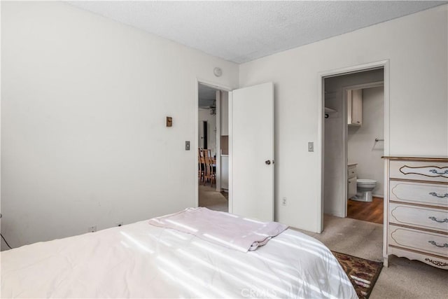 carpeted bedroom featuring ensuite bathroom and a textured ceiling