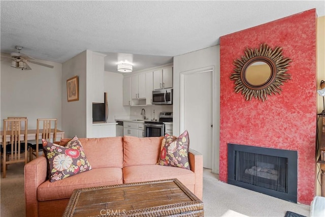 living area with a ceiling fan, light colored carpet, a fireplace, and a textured ceiling