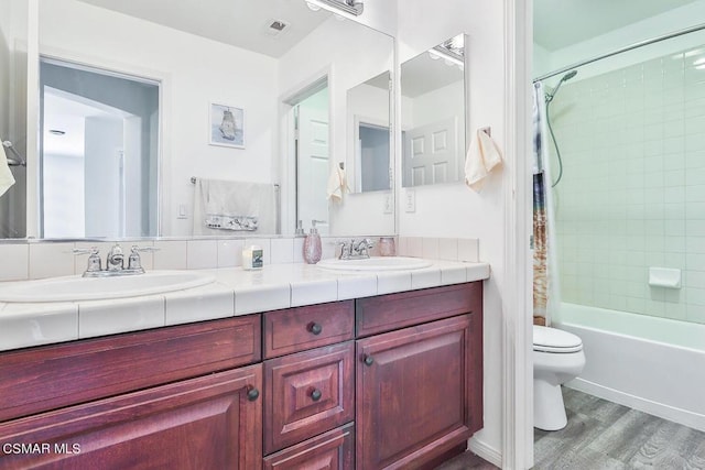 full bathroom with wood-type flooring, toilet, tiled shower / bath combo, and vanity