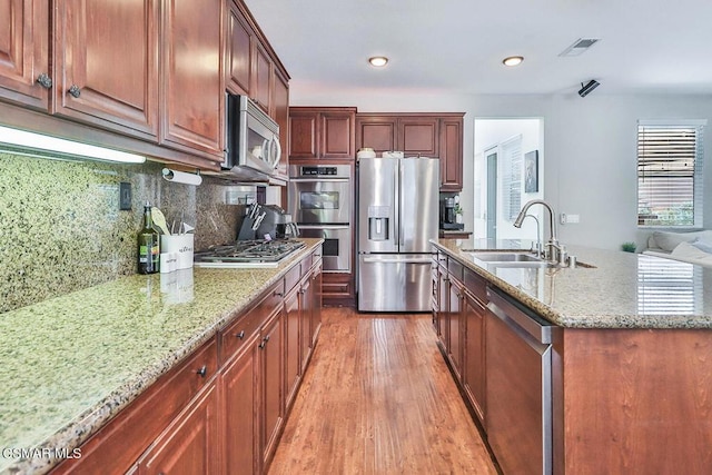 kitchen featuring sink, tasteful backsplash, hardwood / wood-style flooring, stainless steel appliances, and light stone countertops