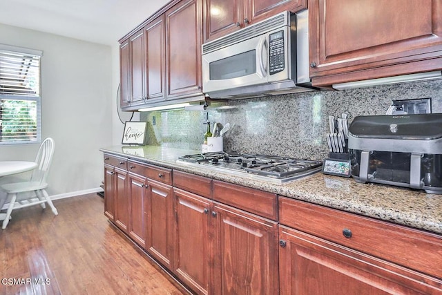 kitchen with decorative backsplash, light hardwood / wood-style flooring, light stone countertops, and appliances with stainless steel finishes