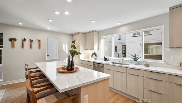 kitchen with sink, a breakfast bar area, a center island, light brown cabinetry, and stainless steel dishwasher