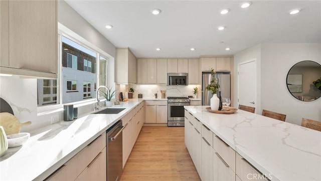 kitchen featuring appliances with stainless steel finishes, tasteful backsplash, sink, light stone counters, and light hardwood / wood-style floors