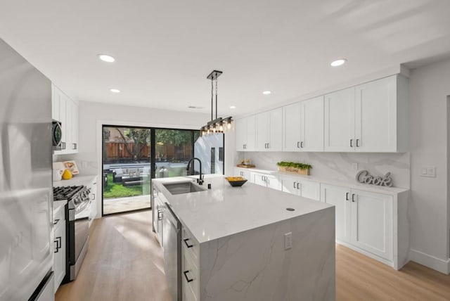 kitchen with appliances with stainless steel finishes, decorative light fixtures, white cabinetry, an island with sink, and sink