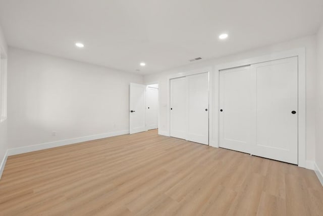 unfurnished bedroom with light hardwood / wood-style floors and two closets