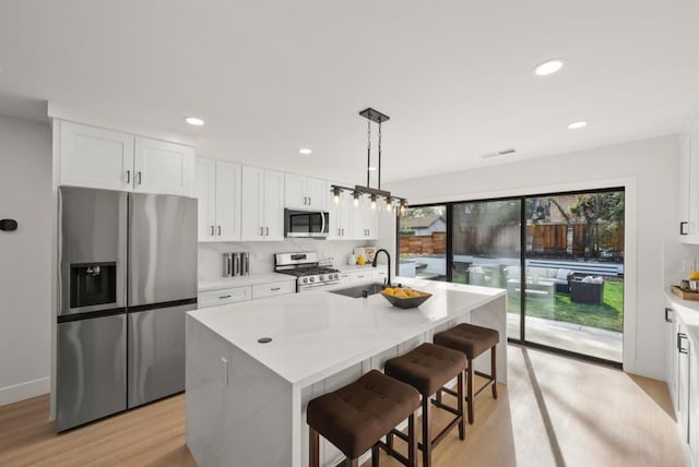 kitchen with white cabinetry, decorative light fixtures, stainless steel appliances, and an island with sink