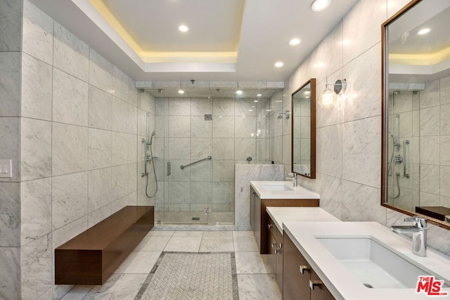 bathroom with a raised ceiling, vanity, tiled shower, and tile walls