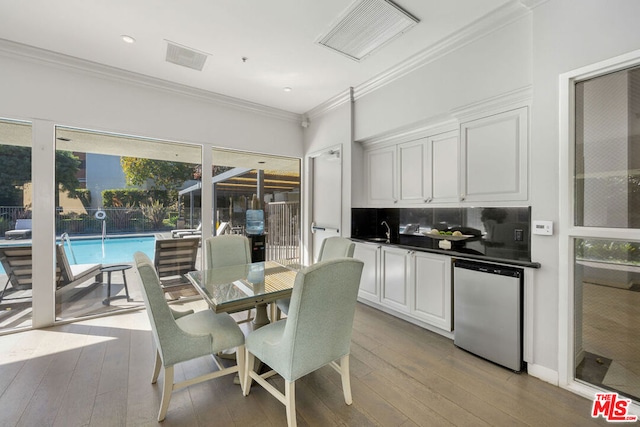 dining area featuring crown molding, beverage cooler, sink, and light wood-type flooring