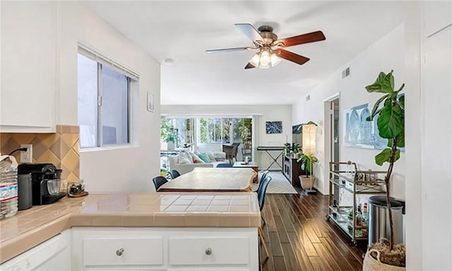 kitchen with ceiling fan, tasteful backsplash, white cabinets, dark hardwood / wood-style flooring, and tile countertops