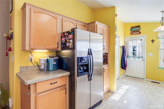 kitchen with pendant lighting, tile counters, stainless steel fridge with ice dispenser, and light brown cabinets