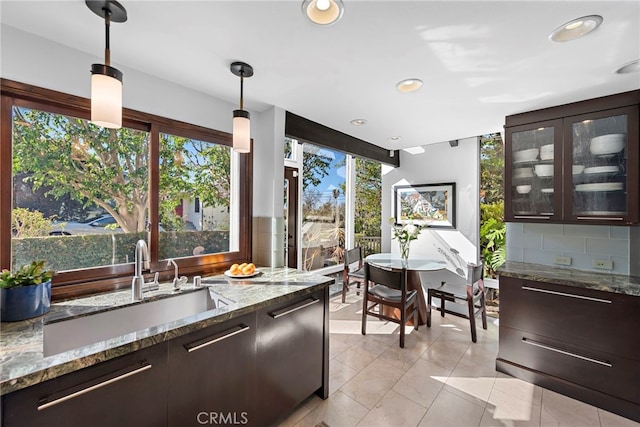 kitchen featuring decorative light fixtures, sink, backsplash, dark brown cabinetry, and light stone countertops