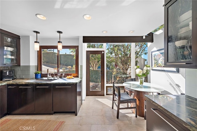 kitchen featuring tasteful backsplash, pendant lighting, dark brown cabinetry, and dark stone counters