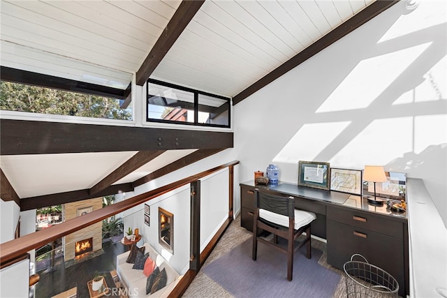 office area featuring a stone fireplace, built in desk, and lofted ceiling with beams