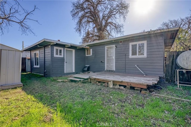 rear view of house featuring a wooden deck, an outbuilding, fence, a yard, and a shed