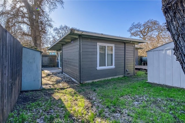 view of side of property featuring a shed, fence, a lawn, and an outbuilding