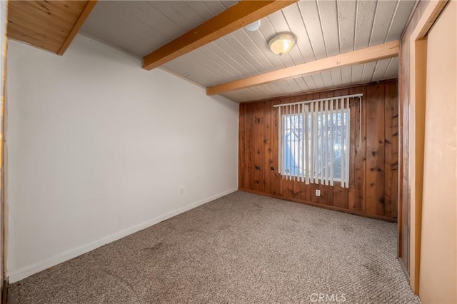 unfurnished room with carpet floors, beamed ceiling, wooden walls, and baseboards