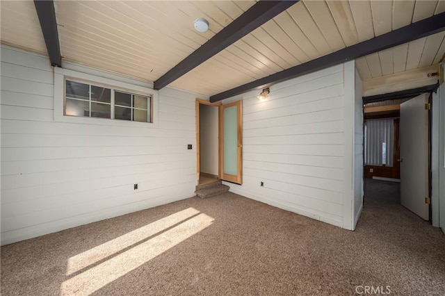 carpeted spare room with beamed ceiling and wooden walls