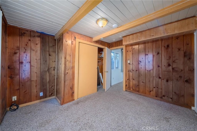 empty room with light colored carpet, beam ceiling, and wood walls