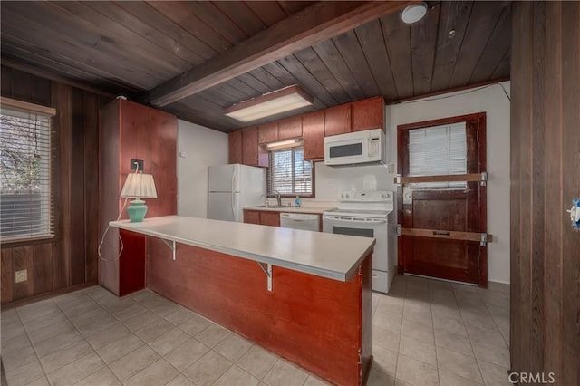 kitchen with wooden walls, a peninsula, white appliances, light countertops, and beamed ceiling