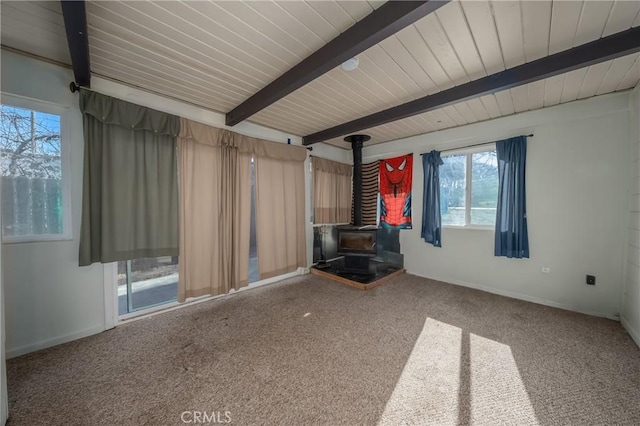 unfurnished living room featuring beam ceiling, carpet floors, and a wood stove