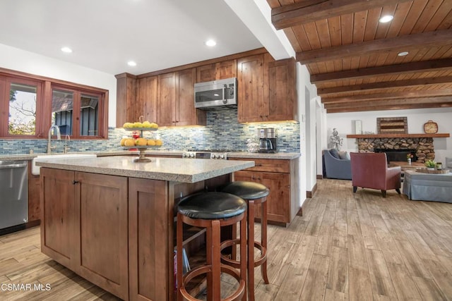 kitchen featuring sink, a kitchen island, beamed ceiling, stainless steel appliances, and light hardwood / wood-style floors