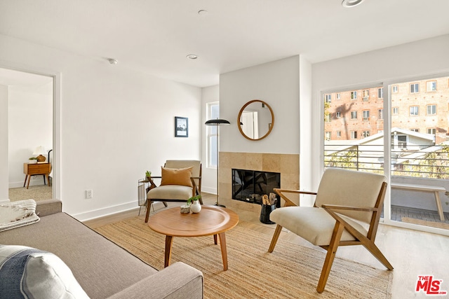 living room with a tile fireplace, a healthy amount of sunlight, and light hardwood / wood-style flooring