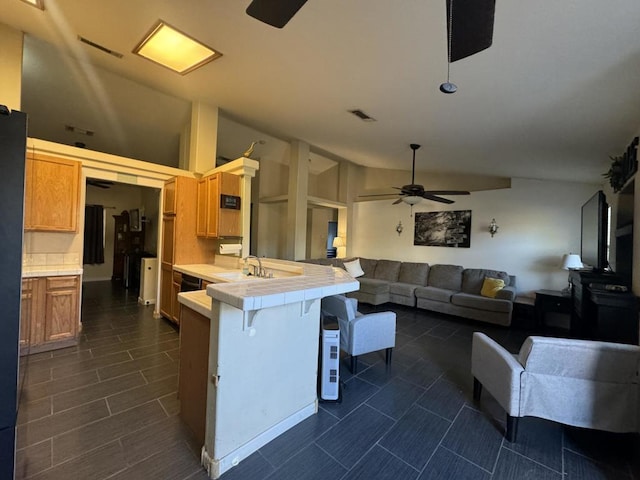 kitchen featuring sink, a kitchen bar, tile counters, ceiling fan, and kitchen peninsula