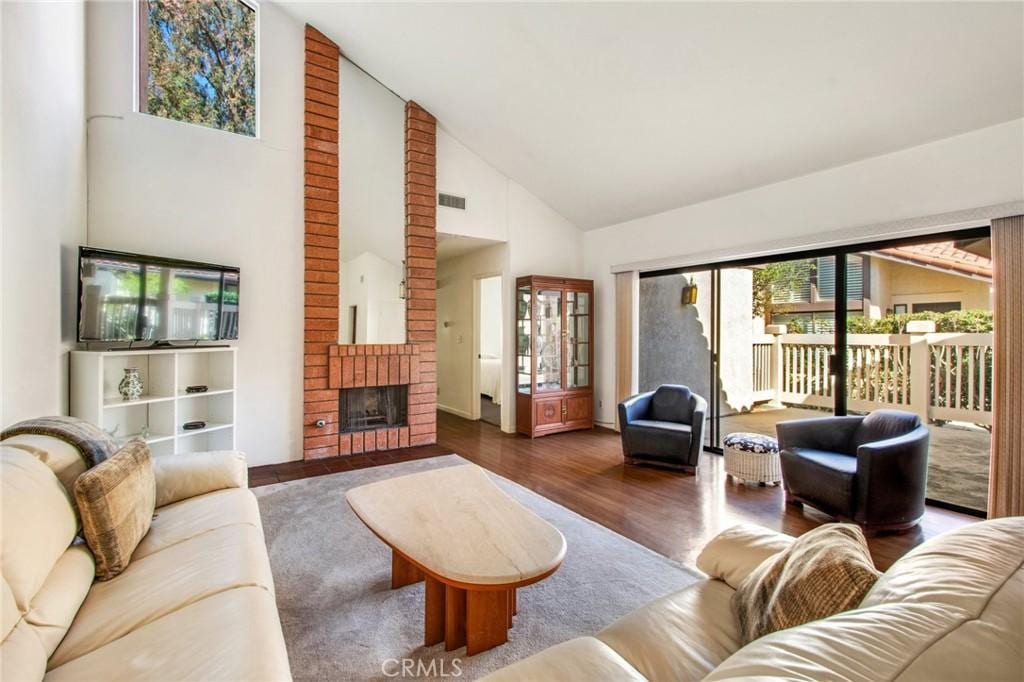 living room with dark hardwood / wood-style flooring, a brick fireplace, and high vaulted ceiling