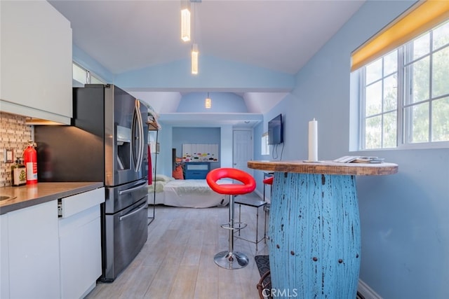 kitchen with decorative light fixtures, white cabinetry, lofted ceiling, a kitchen bar, and light hardwood / wood-style flooring