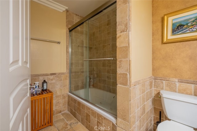 bathroom with bath / shower combo with glass door, ornamental molding, toilet, and tile walls