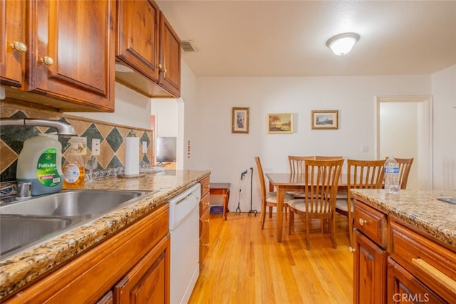 kitchen with white dishwasher, tasteful backsplash, light stone countertops, and light wood-type flooring