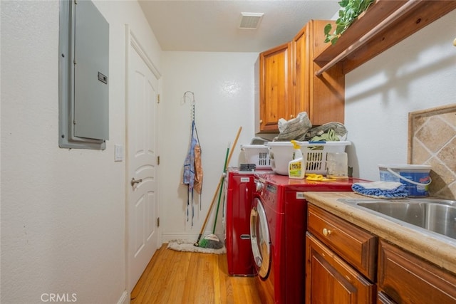 washroom with sink, cabinets, light wood-type flooring, electric panel, and washing machine and dryer