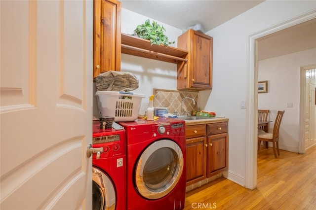 clothes washing area featuring cabinets, separate washer and dryer, sink, and light wood-type flooring