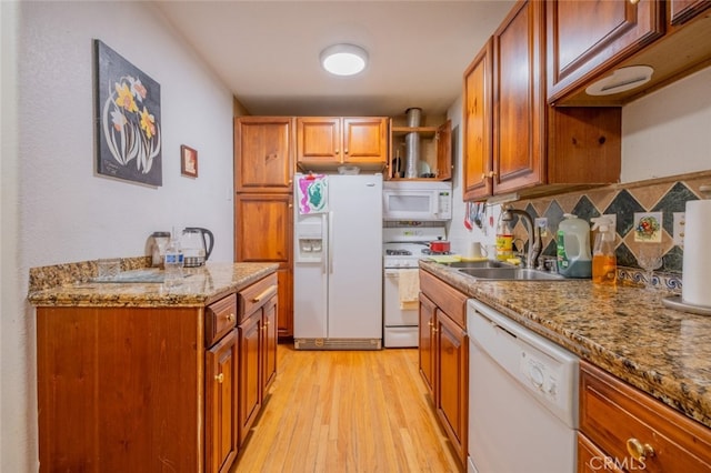 kitchen featuring sink, light stone counters, light hardwood / wood-style flooring, white appliances, and decorative backsplash