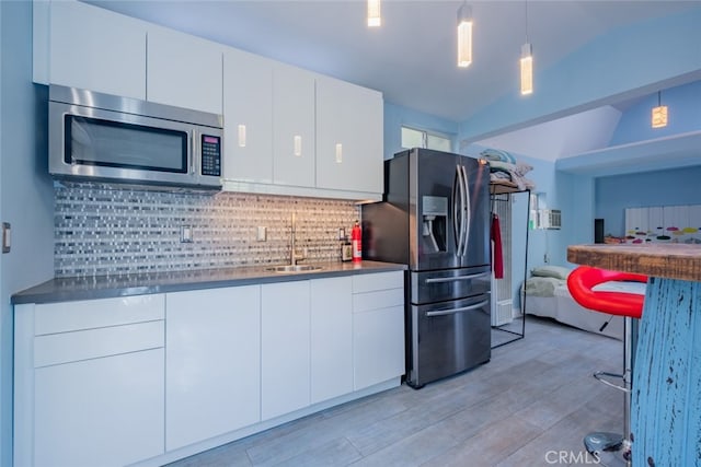 kitchen with vaulted ceiling, appliances with stainless steel finishes, pendant lighting, white cabinetry, and decorative backsplash